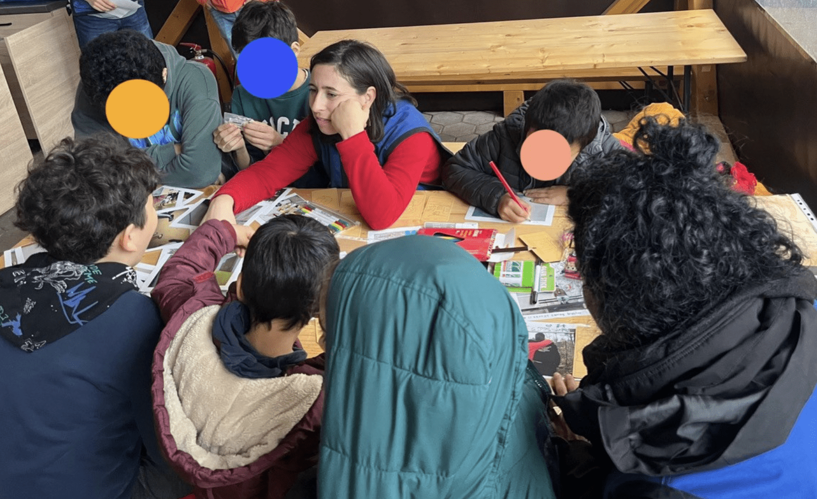 Erica Belli, the facilitator, sits at a table with youth participants, discussing printed photos and working on creative captioning