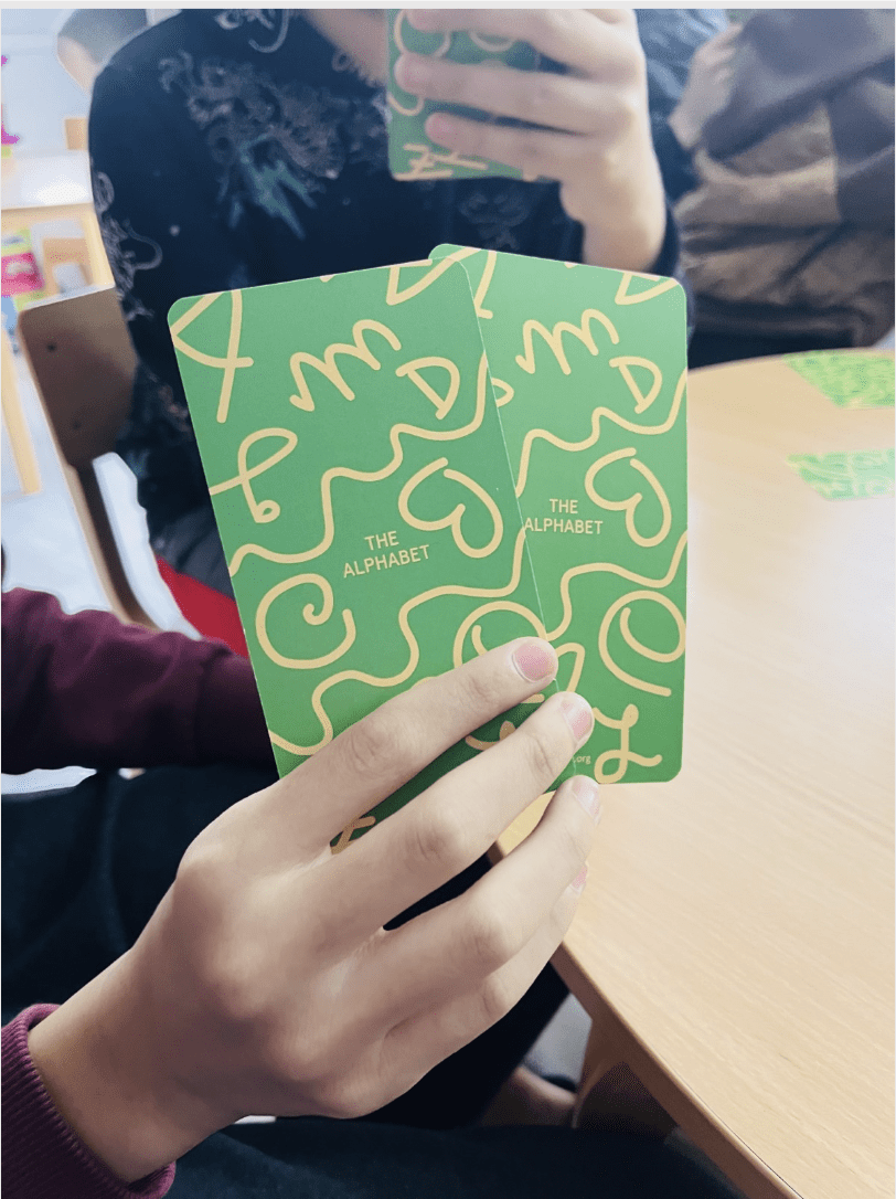 2 people holding green and yellow cards, showing the back of the cards from the alphabet card game